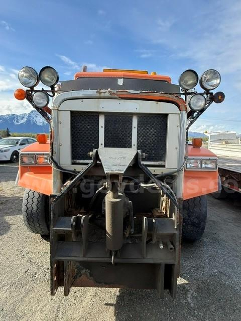 Front view of orange 2002 Freightliner FLD120 dump truck showing grille, bumper, and heavy-duty hitch/prod attachment with multiple lights.