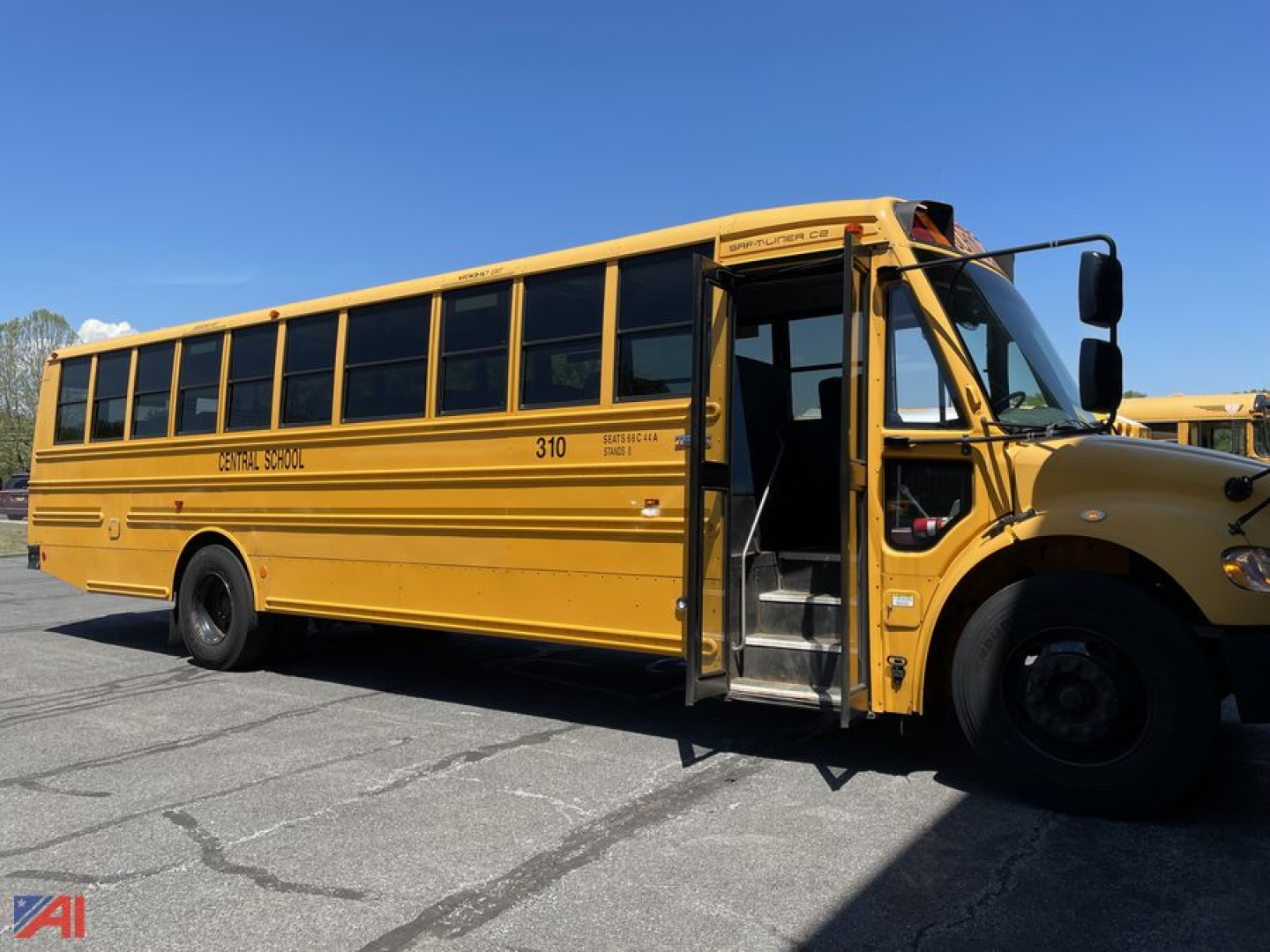School bus side view showing yellow Freightliner C2 with open entry door, black tires, and windowed body. Visible text includes 'CAPITAL SCHOOL' or similar on side and '310' near front.