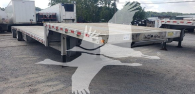 Flatbed trailer showing low deck with drop deck, metal surface, support legs, and reflector stripes along edge; visible wheels and adjacent trailers in a lot.