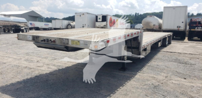 Flatbed trailer with drop deck showing low-profile frame and dual axle setup in an open yard.