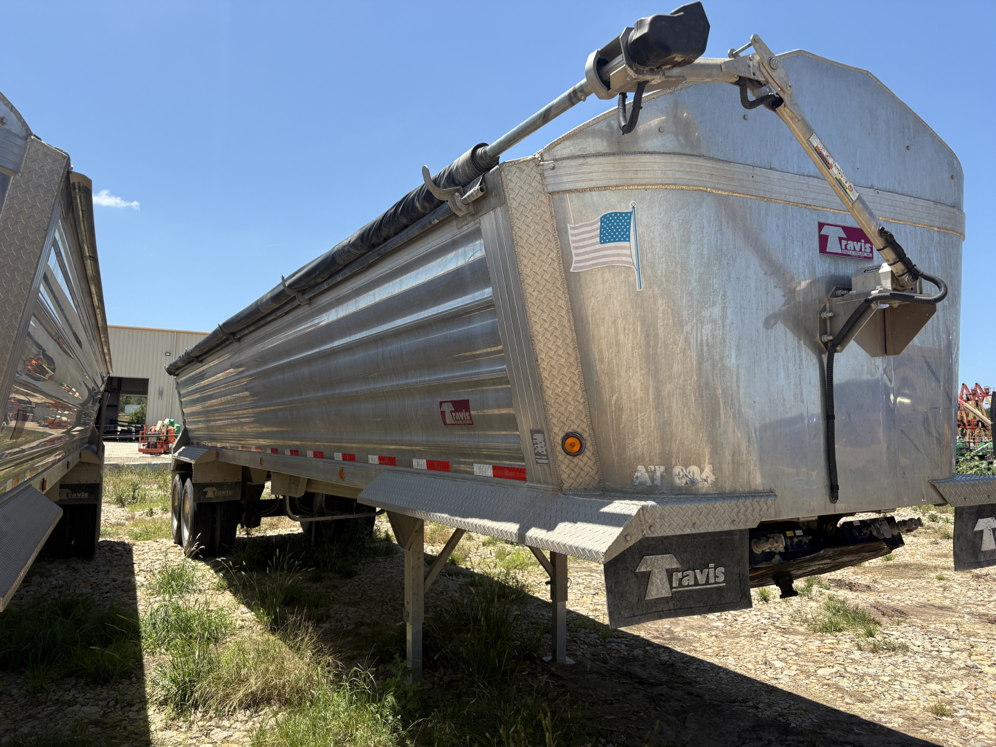 Dump trailer showing side view and front nose with metal diamond plate, Travis label, and support legs visible.