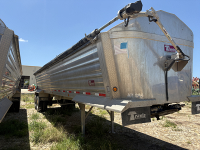 Dump trailer showing side view and front nose with metal diamond plate, Travis label, and support legs visible.