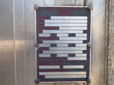 Metal identification plate on Travis dump trailer showing manufacturing data: MFG BY TRAVIS BODY & TRAILER, INC. Houston, TX; Date of MFG NOV 2023; GVWR 6800; GAWR front/dual 20000? (illegible); model field and VIN partially visible; variou