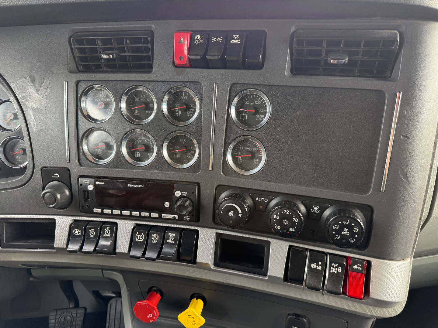 Kenworth T680 dash panel showing multiple gauges, switches, and control knobs in a truck interior. Includes climate controls and stereo unit.