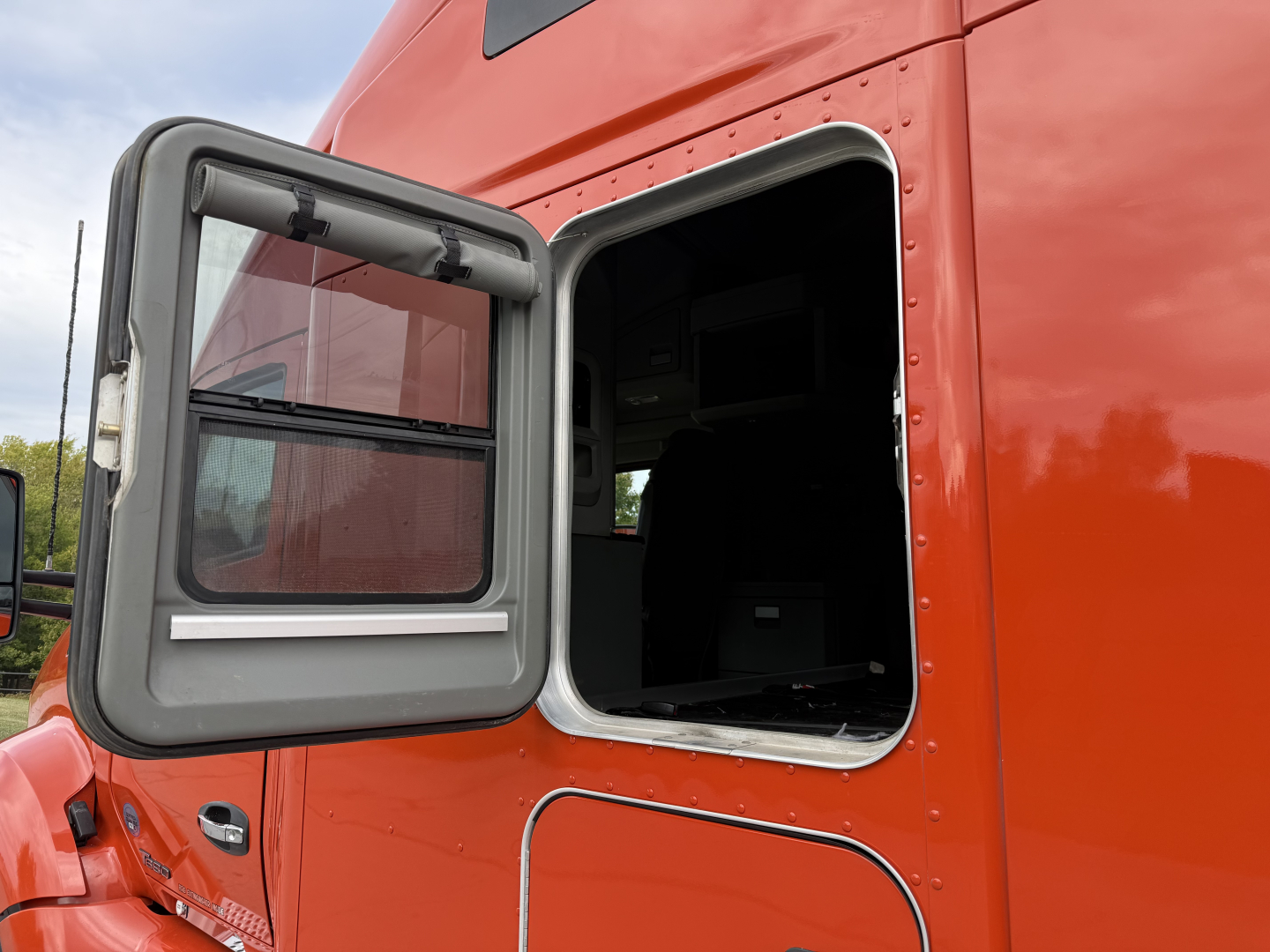 Kenworth T680 sleeper cab side door open revealing interior cab window and orange paint