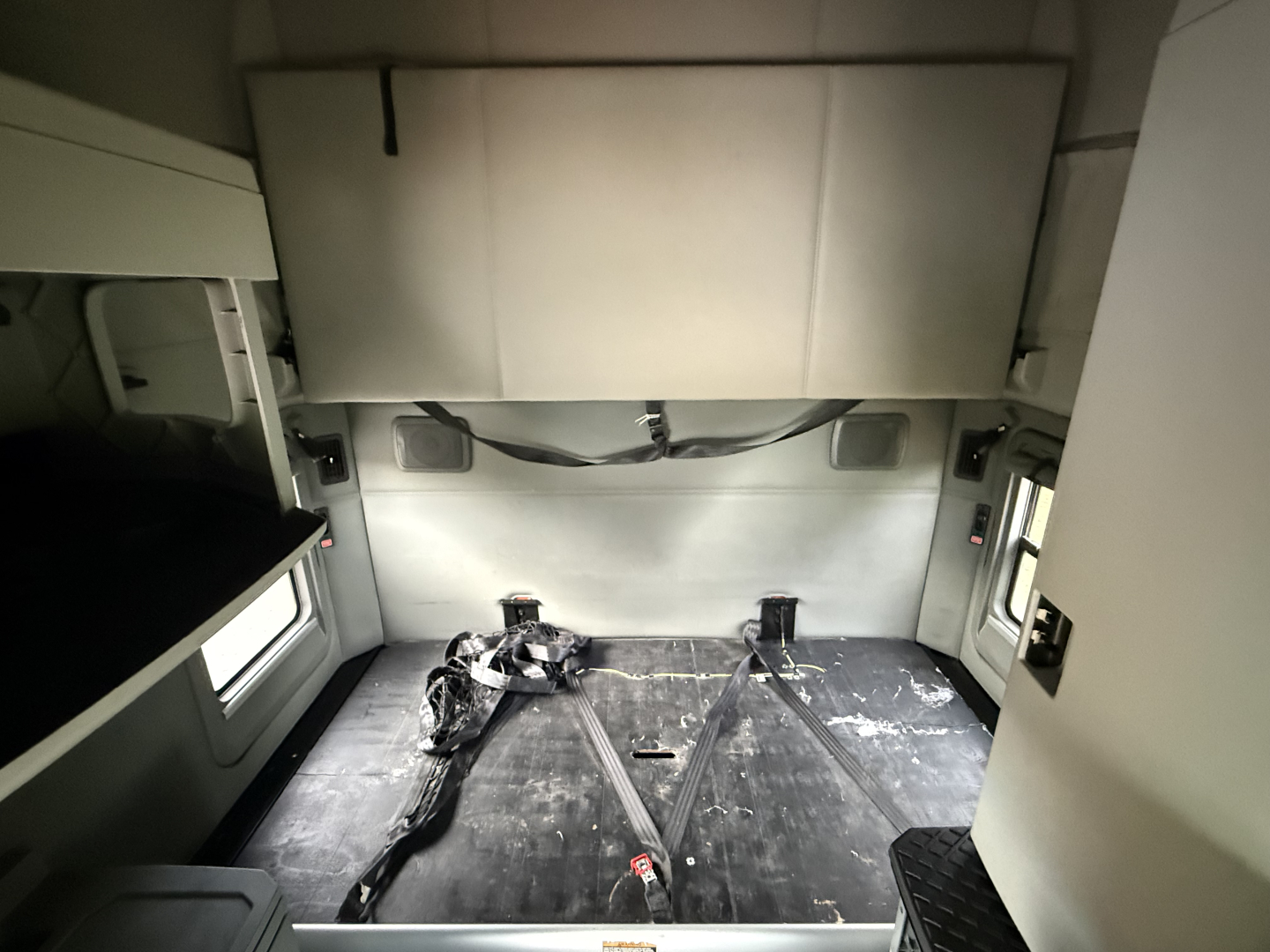 Kenworth T680 sleeper cab interior cargo area with rear seating removed showing flat bed and straps across, cargo area with window on left and right, overhead bunk compartment visible