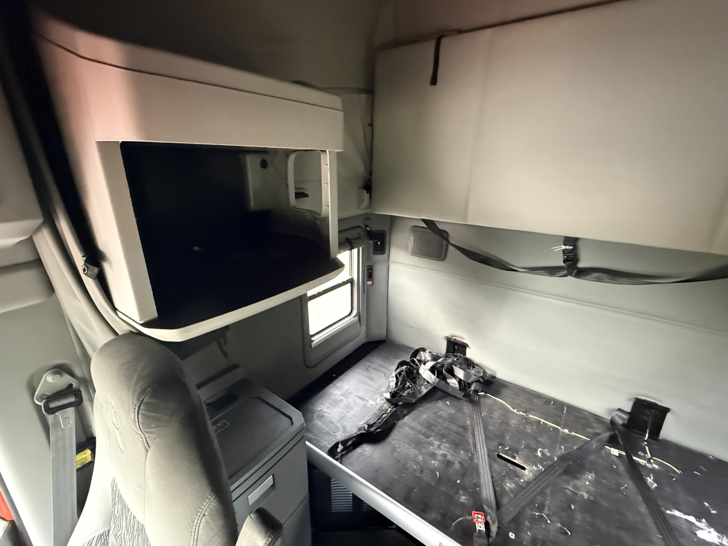 Kenworth T680 sleeper cab interior with seating area and overhead storage shelf visible.