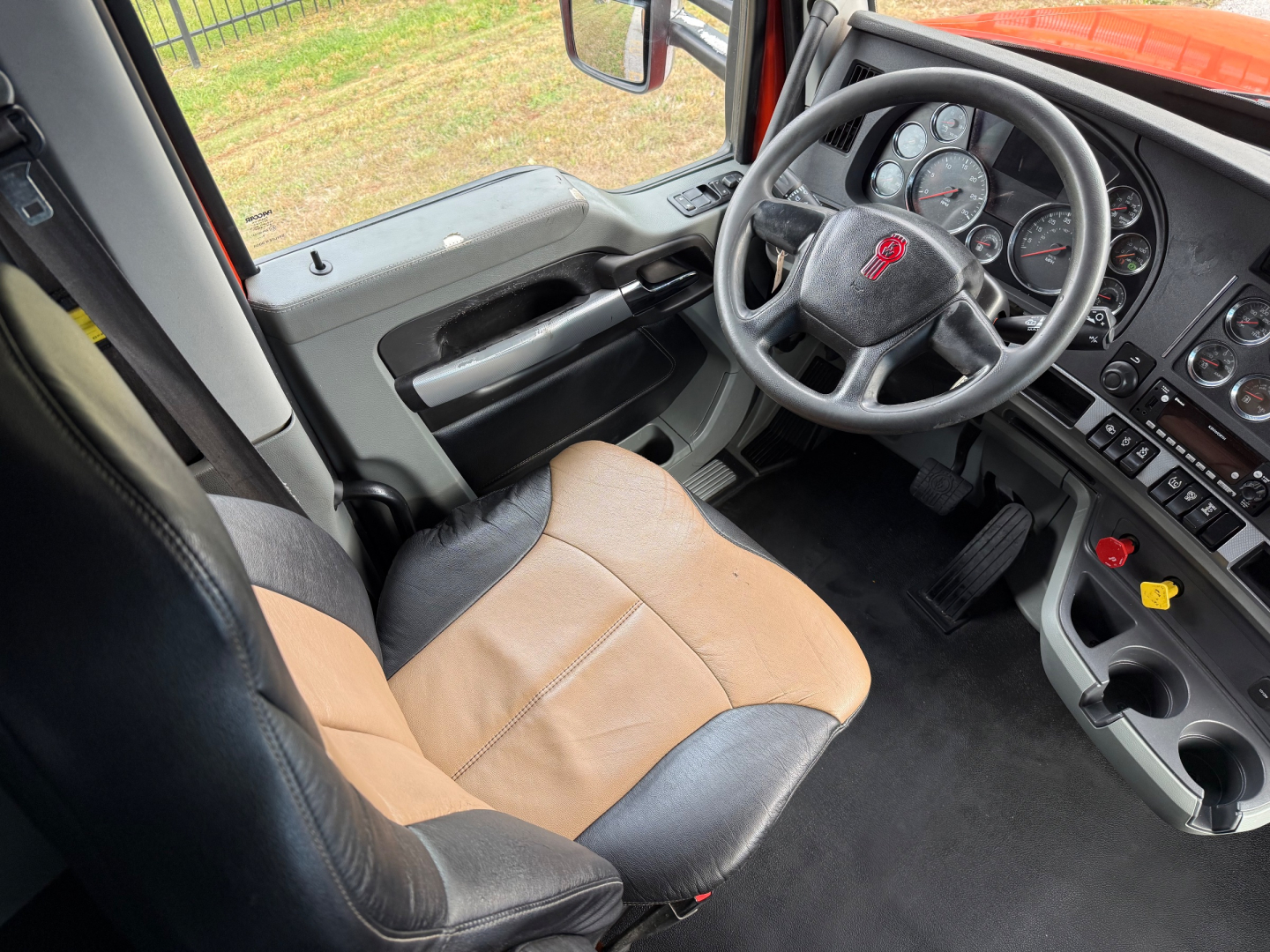 Truck cab interior of a 2021 Kenworth T680 showing steering wheel, dashboard gauges, driver seat, and center console.