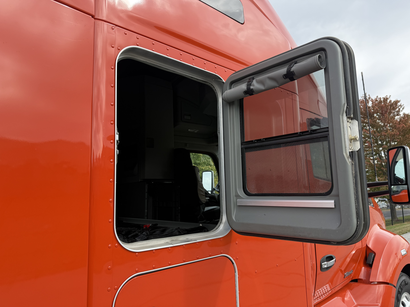 Kenworth T680 truck cabin window open showing side door opening and orange paint.