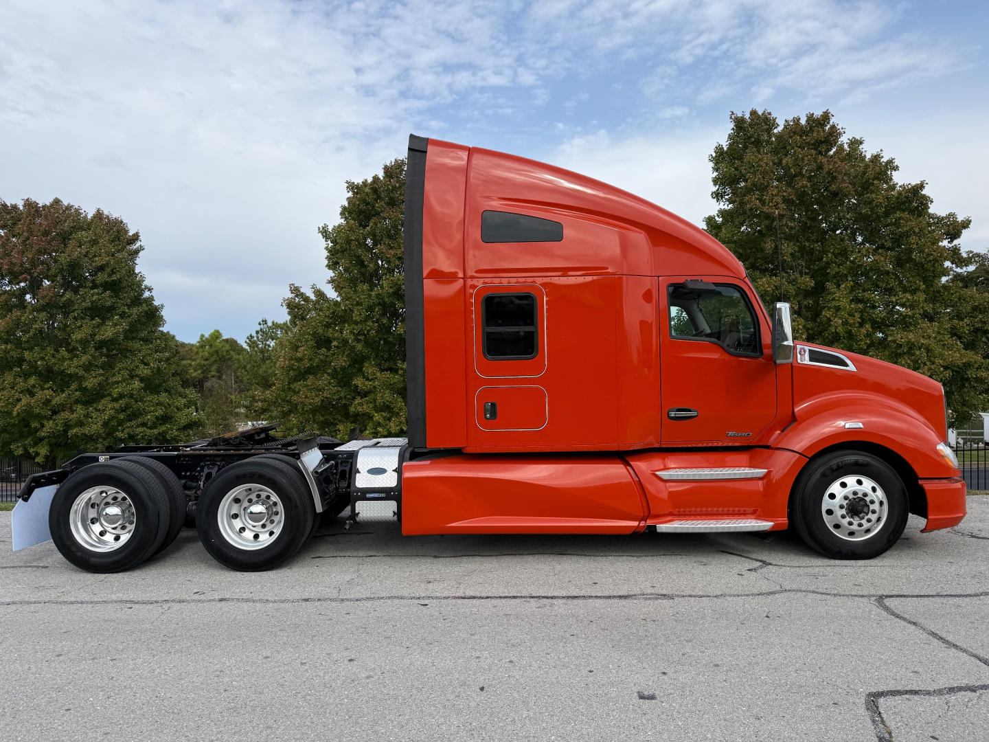 Kenworth T680 sleeper cab tractor truck in orange, side view showing 10-wheel configuration, windows, and aerodynamic cab profile.