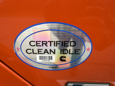 Certified Clean Idle oval sticker on orange Kenworth truck door with barcode and small text.