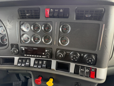 Kenworth T680 dash panel showing multiple gauges, switches, and control knobs in a truck interior. Includes climate controls and stereo unit.