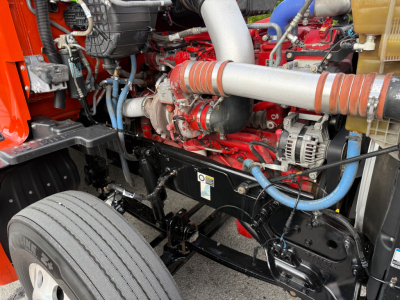 Kenworth T680 engine bay showing large turbo intake, red engine block, blue hoses, and black chassis with label placard.
