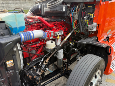 Kenworth T680 engine bay showing red engine, blue coolant reservoir, air intake, hoses, and electrical wiring.
