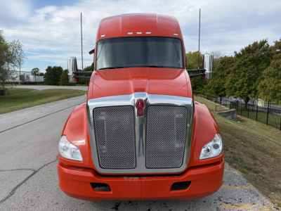 Kenworth T680 front view showing chrome grille and orange cab, headlights, and side mirrors.