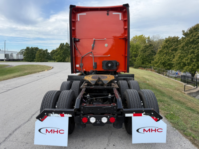 Kenworth T680 rear view showing chassis and fifth wheel area, orange cab back, twin rear axles, mud flaps with MHC logo, and tail lights.