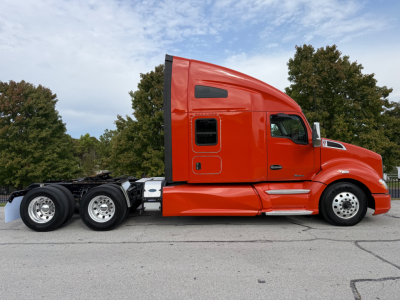 Kenworth T680 sleeper cab tractor truck in orange, side view showing 10-wheel configuration, windows, and aerodynamic cab profile.