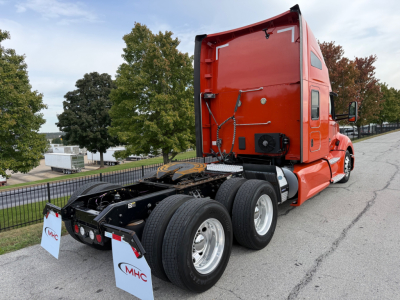 Kenworth T680 tractor from side/rear showing red sleeper cab, dual rear axles, fifth wheel, and bumper with CMHC signs.