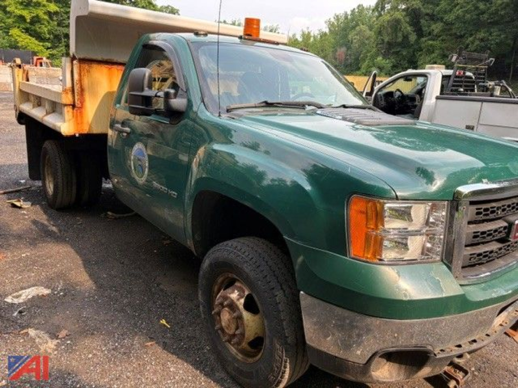 GMC Sierra 3500 dump truck in green with an orange warning light on top, visible front grille, and rusted flatbed. VIN 1GD322CG2CF228851 visible in listing.