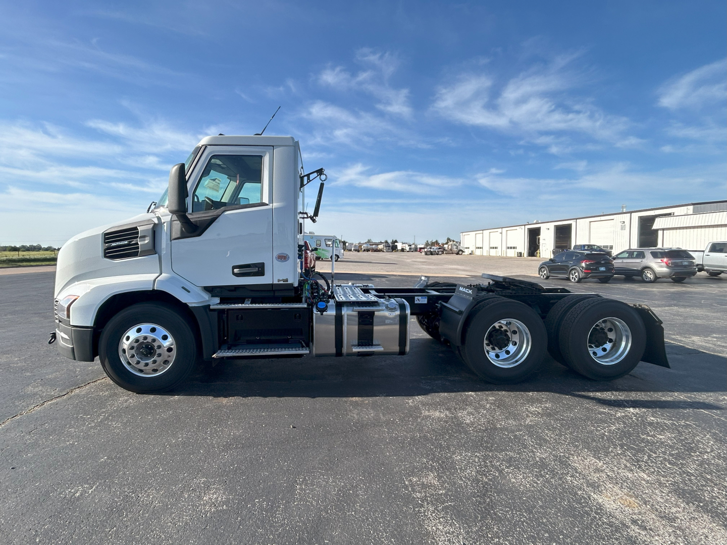 Side view of a white 2027 Mack AN64T conventional daycab truck chassis showing cab, fuel tanks, exhaust, and rear axles.