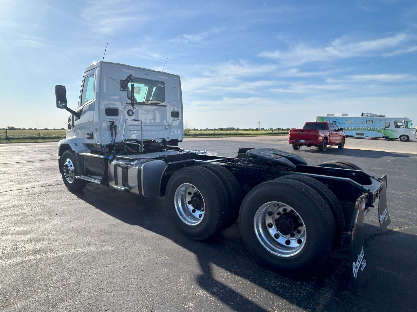 Truck cab and chassis showing tandem rear axles on a 2027 Mack AN64T with white cab and black chassis in an open lot.