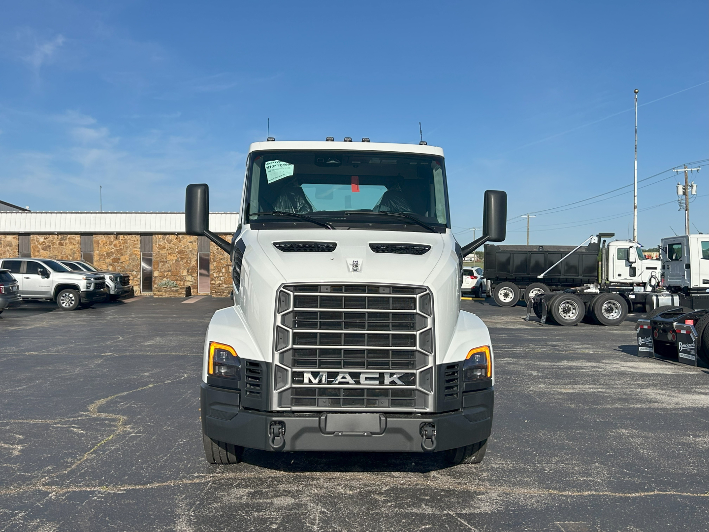 Front view of a white 2027 Mack AN64T daycab with large grille and black bumper, showing Mack emblem, headlights, and side mirrors.