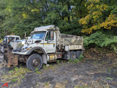 2012 International SF537 WorkStar dump truck in in-service condition, white cab with yellow stripes, dump bed, front-mounted plow, visible number 44, rugged tires, set in a gravel lot with trees.