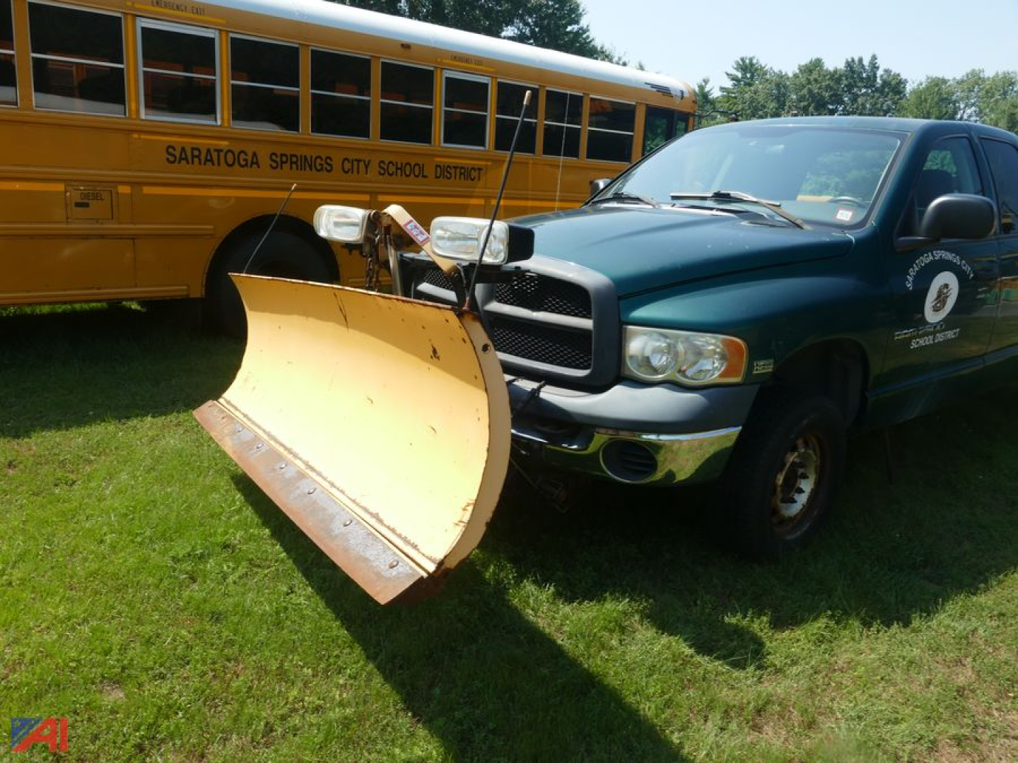 2003 Dodge Ram 2500 Quad Cab with plow attachment in front of yellow school bus on grass.