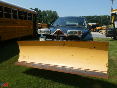 Front view of a 2003 Dodge Ram 2500 quad cab with a large yellow snow plow attached to the front. School bus in background and grassy lot.