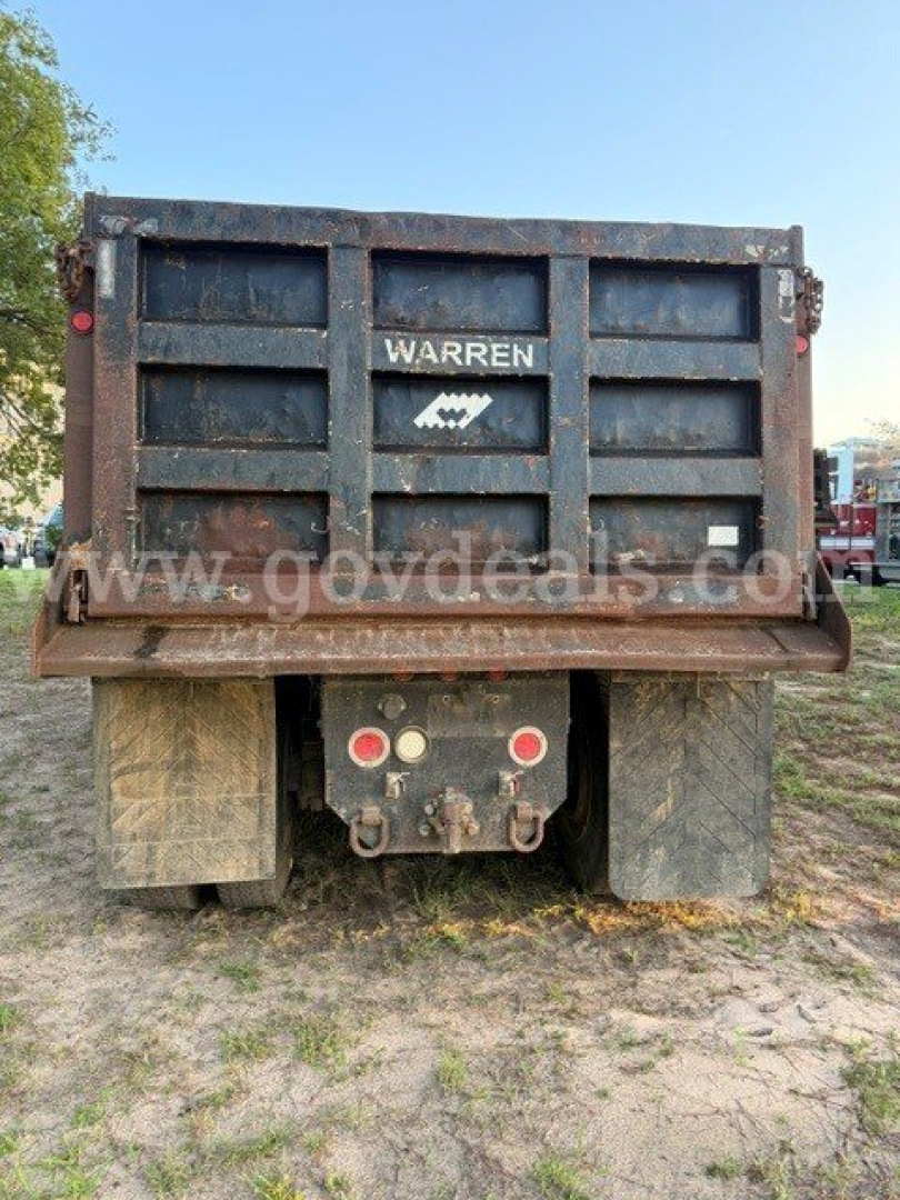 Warren dump truck bed showing rear with branding and taillight assemblies, dirt and mud on tires.
