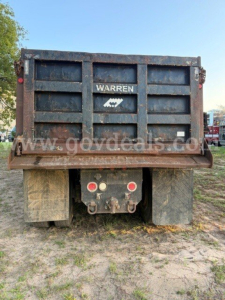 Warren dump truck bed showing rear with branding and taillight assemblies, dirt and mud on tires.