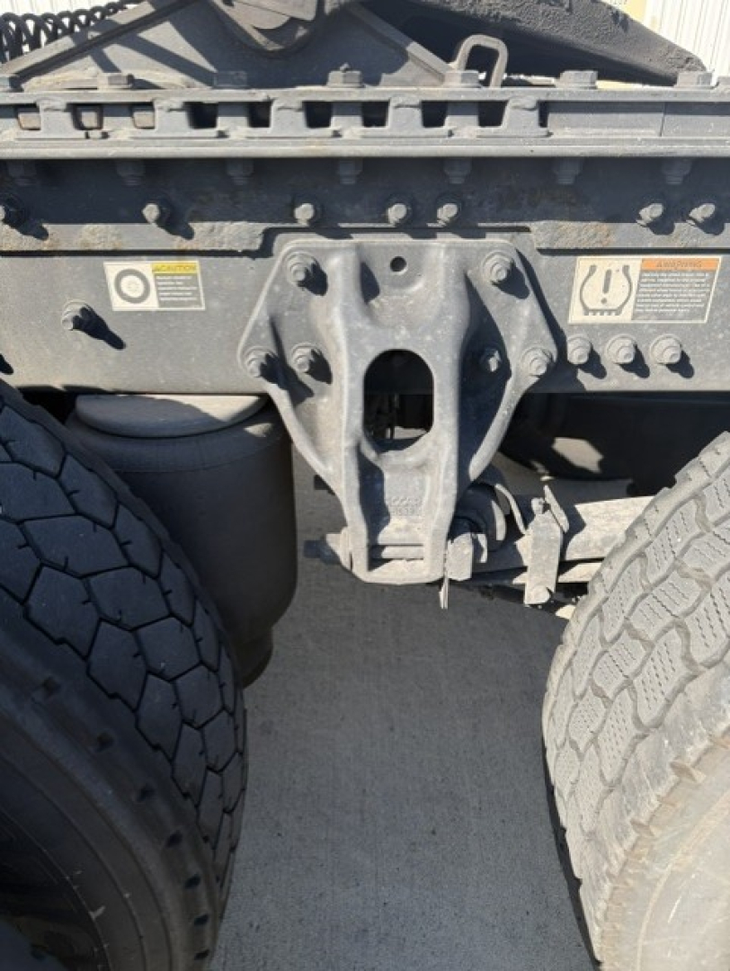 Kenworth T680 rear chassis showing fifth wheel mounting bracket and dual rear tires, with warning labels on frame and hitch area.