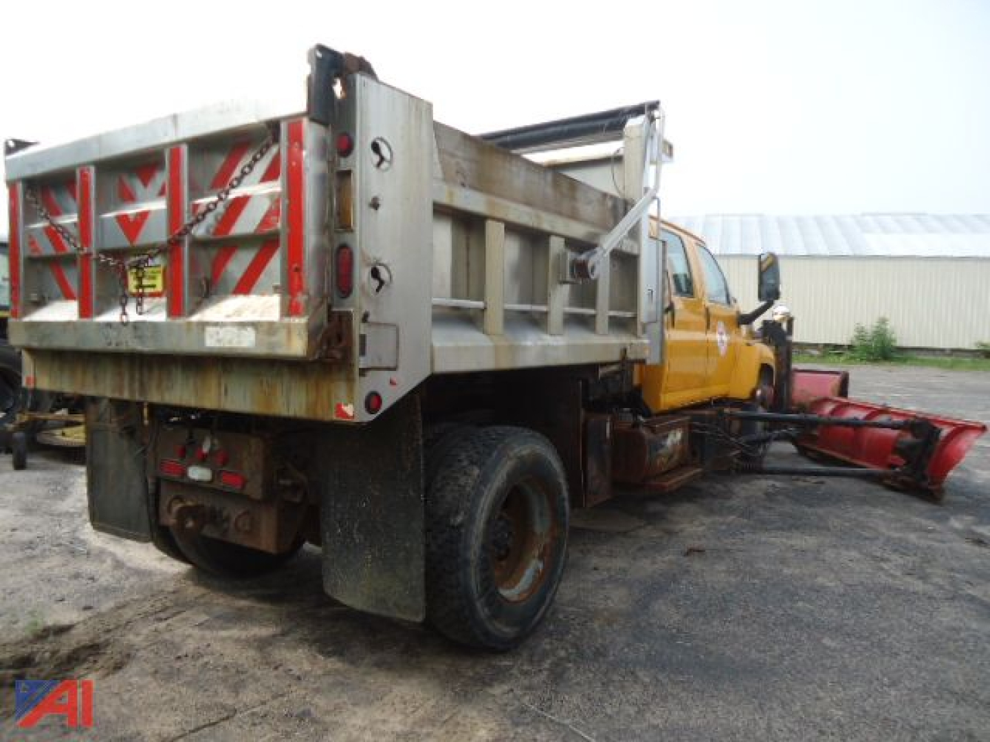 Dump truck chassis with plow attachment and striped rear gate, side view showing metal dump bed and yellow cab.