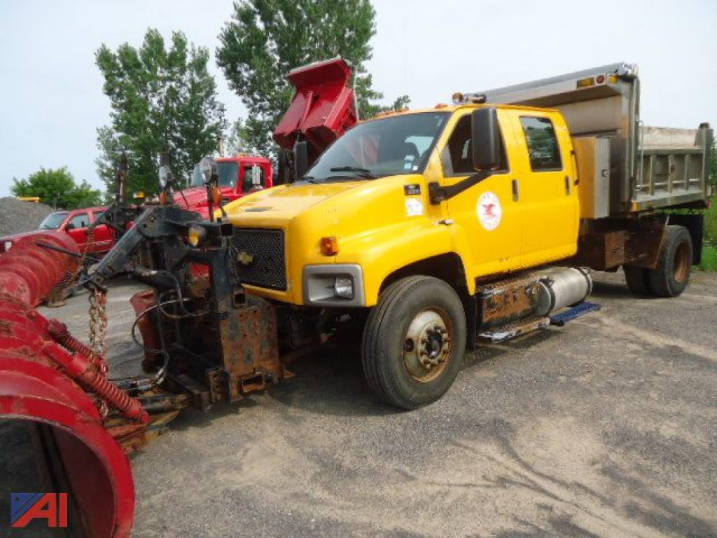 Yellow 2007 Chevrolet Kodiak C8500 dump truck with plow and dump bed, view of front-left side showing plow at front, large side mirrors, diesel fuel tanks, and utility equipment.