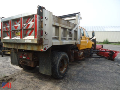 Dump truck chassis with plow attachment and striped rear gate, side view showing metal dump bed and yellow cab.