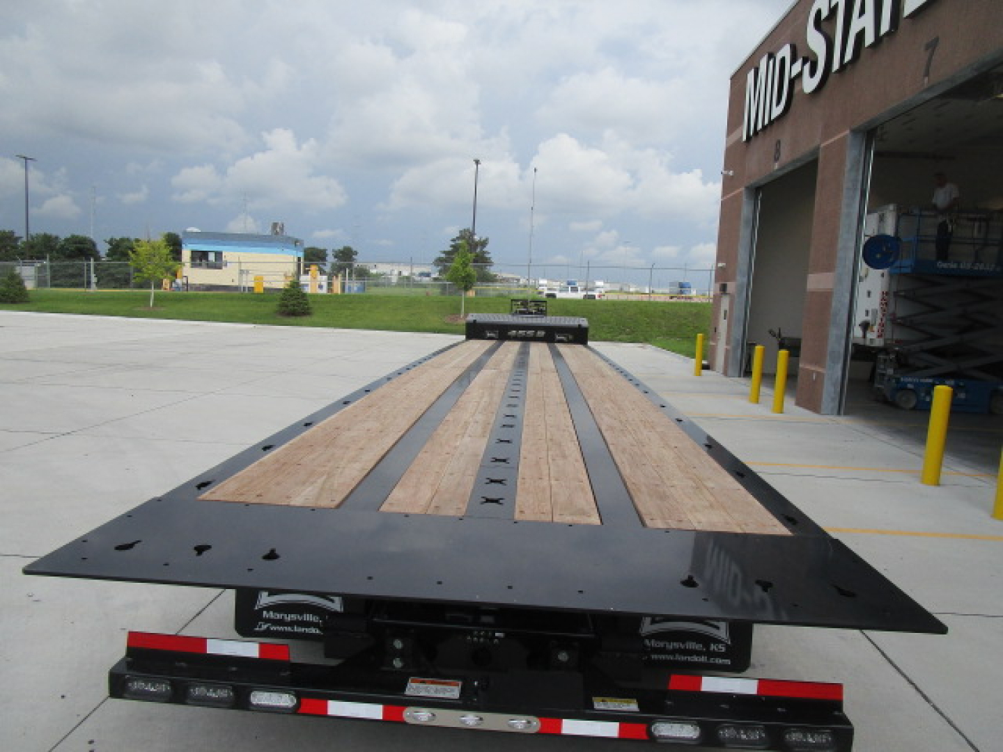 Flatbed trailer with wooden deck and black steel frame extending toward camera.