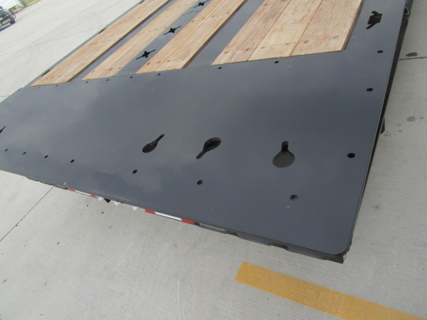 Flatbed trailer deck showing black steel frame with wooden planks and multiple cutouts for chains and pins.