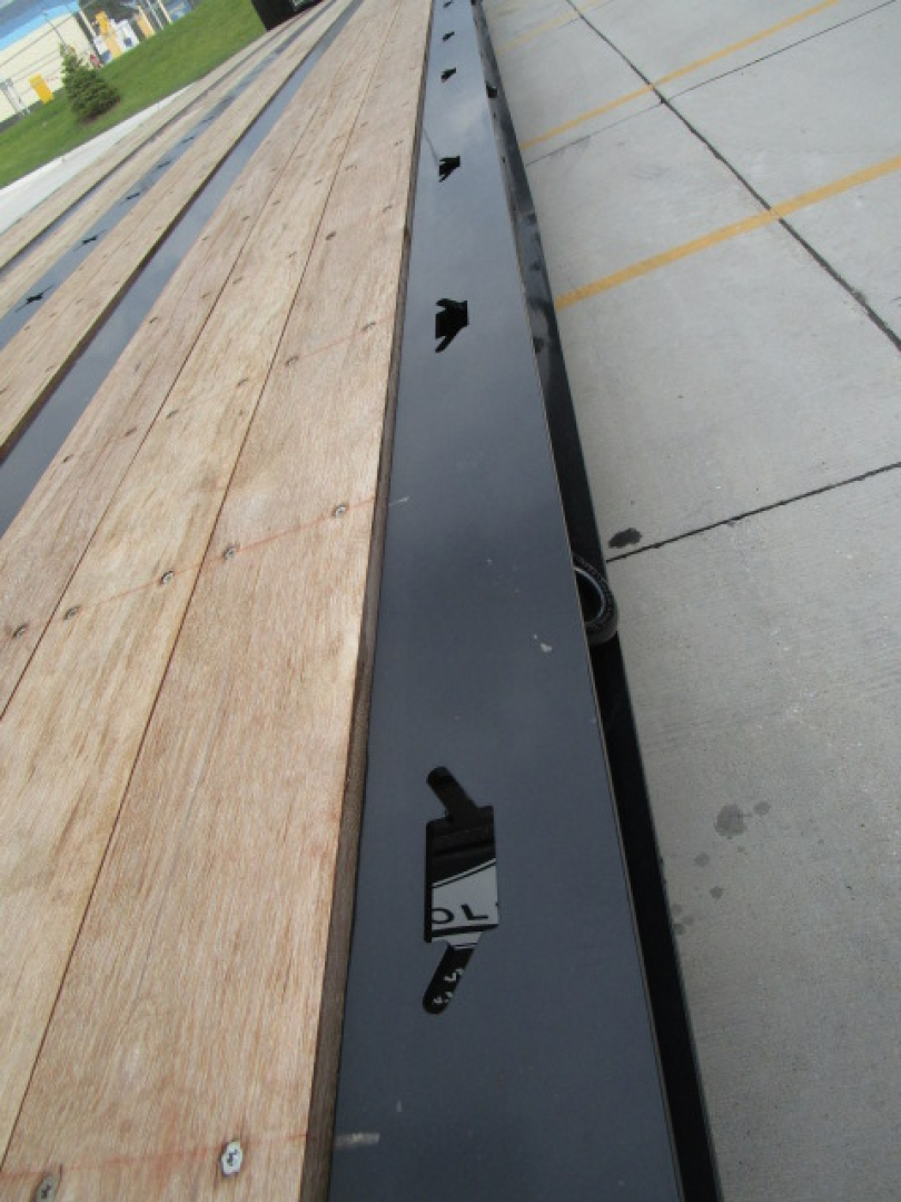 Trailer axle beam and wooden deck of 2026 Landoll 455 traveling axle trailer with black frame and holes for decking hardware.