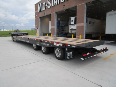 Landoll trailer with long flatbed and dual rear axles parked near a mid-states facility, showing loading ramp, wooden deck, and tire wheels.