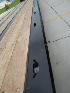 Trailer axle beam and wooden deck of 2026 Landoll 455 traveling axle trailer with black frame and holes for decking hardware.