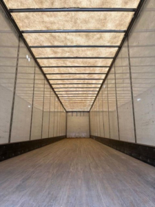Trailer interior showing long empty cargo space with wooden floor and translucent roof panels.