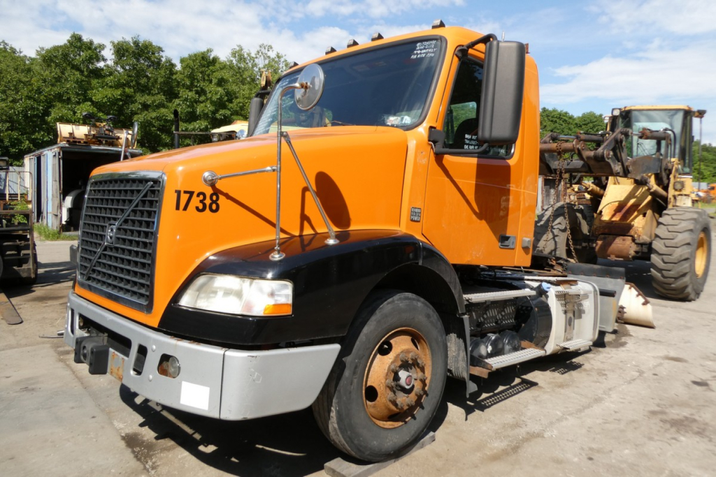 Orange 2012 Volvo VNM42T conventional daycab truck with number 1738 on cab side, front view, black bumper and side mirrors, parking lot.