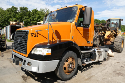 Orange 2012 Volvo VNM42T conventional daycab truck with number 1738 on cab side, front view, black bumper and side mirrors, parking lot.