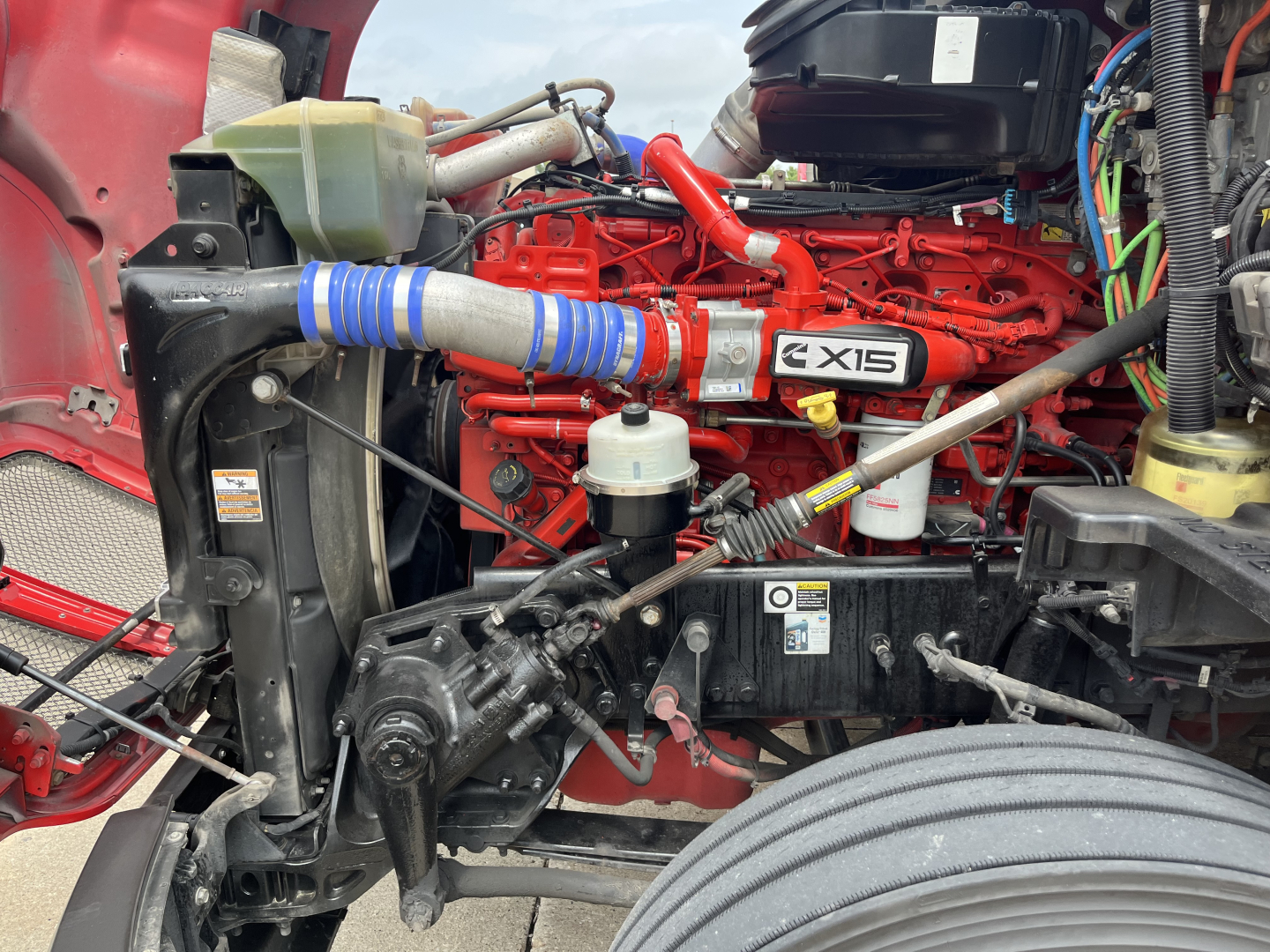 Kenworth T680 engine bay showing X15 badge on engine cover and red engine block with blue silicone intercooler hose.