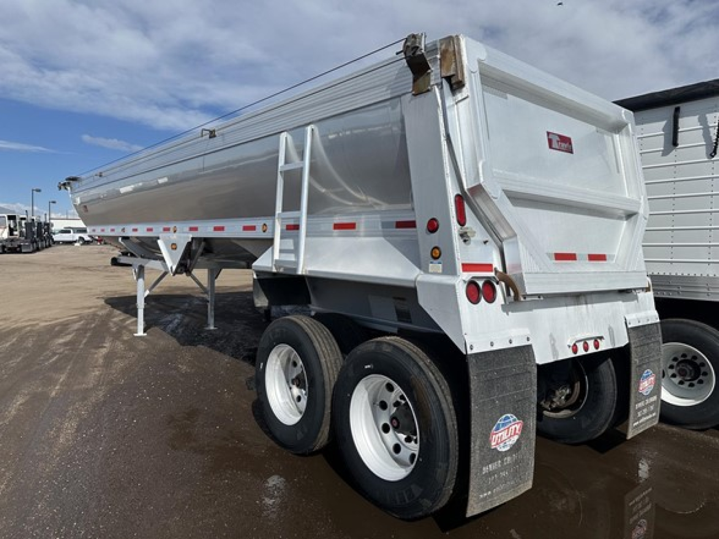 End dump trailer showing frameless aluminum body and dual rear axles with white wheels.