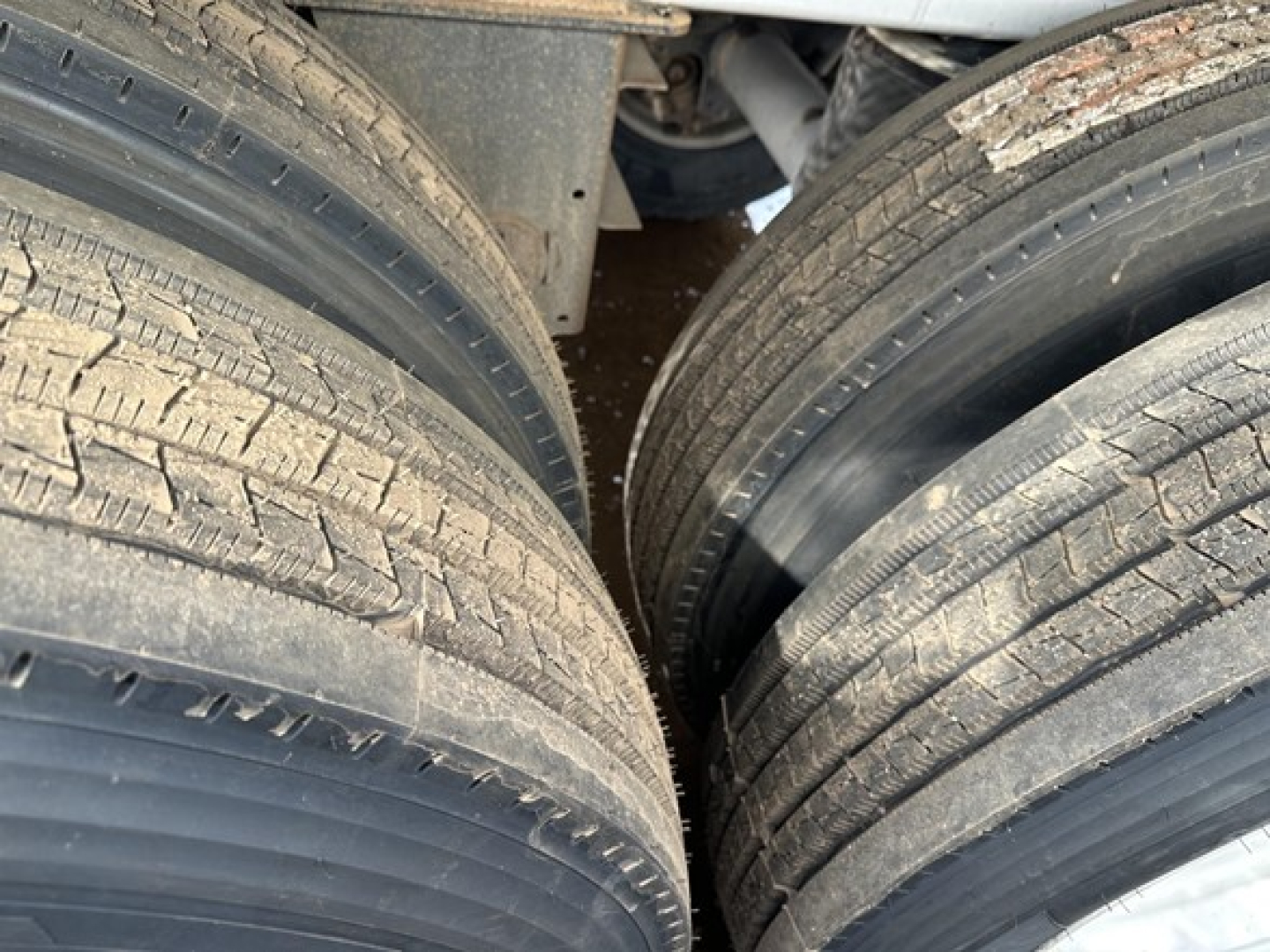 End dump trailer wheel area showing dual tires and part of frame. Visible tread pattern on tires and a portion of aluminum trailer structure.