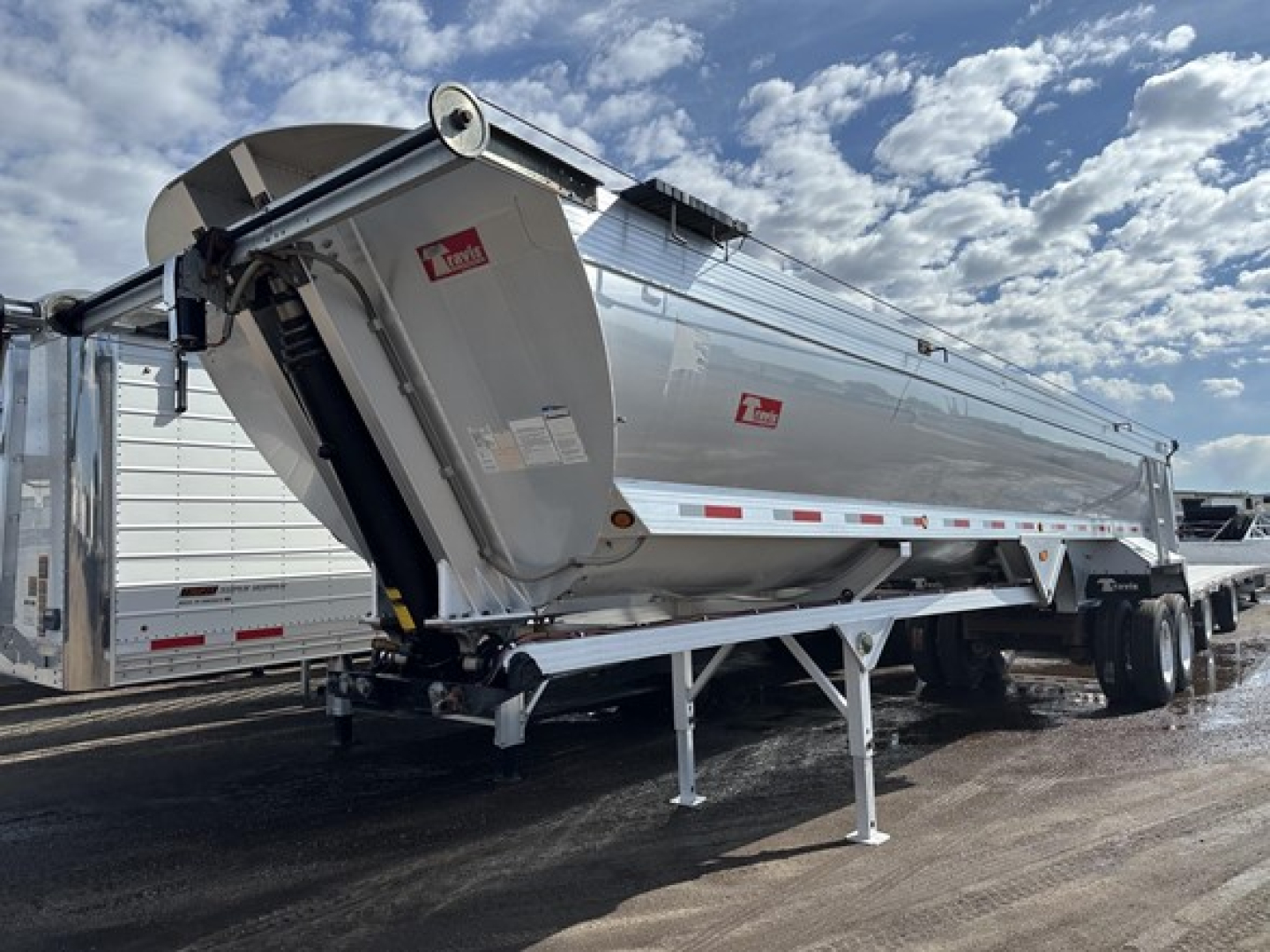 Travis frameless aluminum end dump trailer in side angle view showing long silver cylindrical body with hydraulic hoist and landing gear.