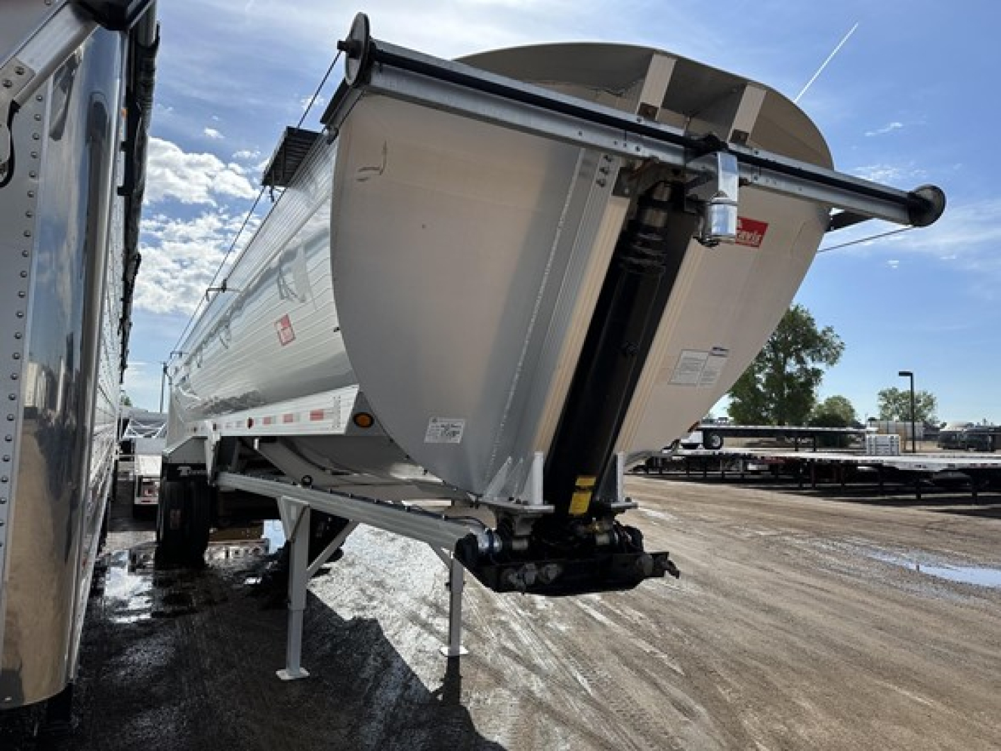 Travis frameless aluminum end dump trailer in side-front view showing lift mechanism and rear discharge area.