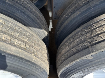 Trailer axle tires in close-up view under a frameless aluminum end dump trailer showing paired dual wheels on both sides.