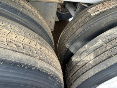 End dump trailer wheel area showing dual tires and part of frame. Visible tread pattern on tires and a portion of aluminum trailer structure.